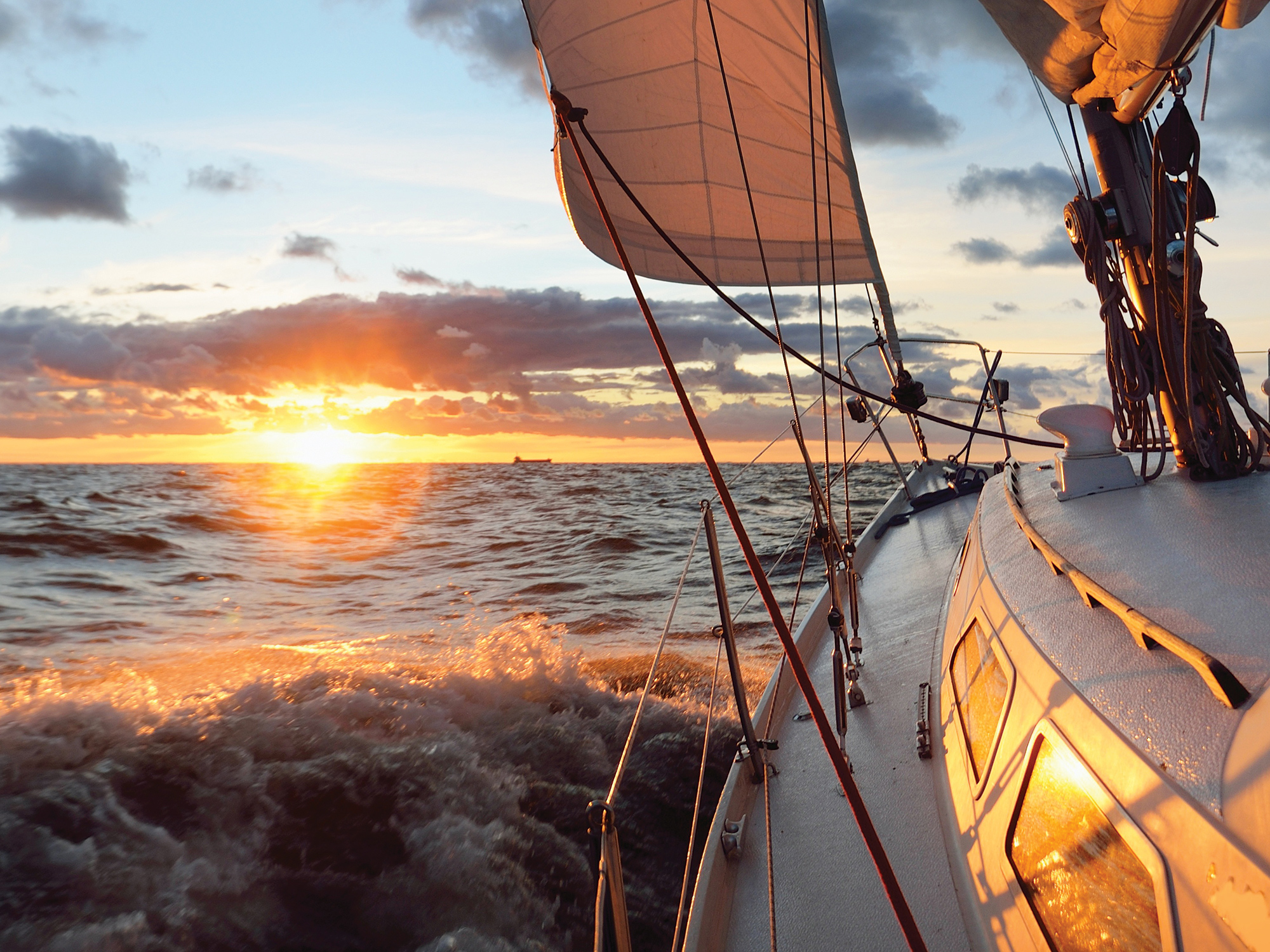 Yacht sailing in an open sea at sunset.