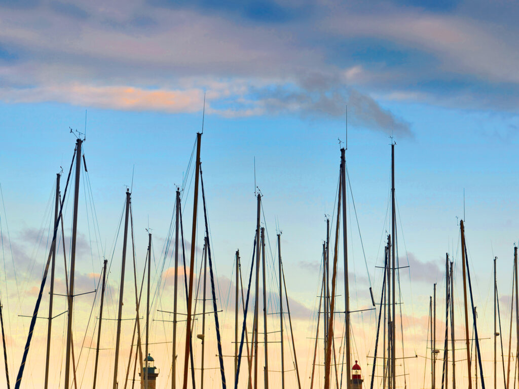 closeup view of row of sailboat masts in a harbor under a colorful cloudy sky