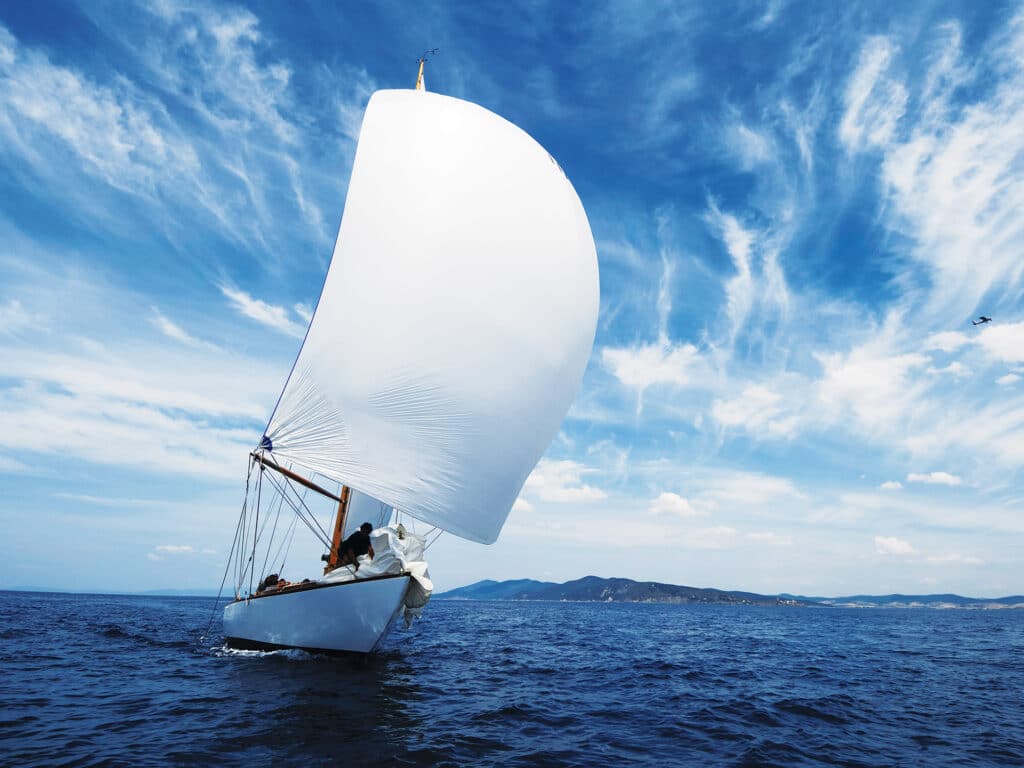 vintage sailboat with white spinnaker sailing downwind